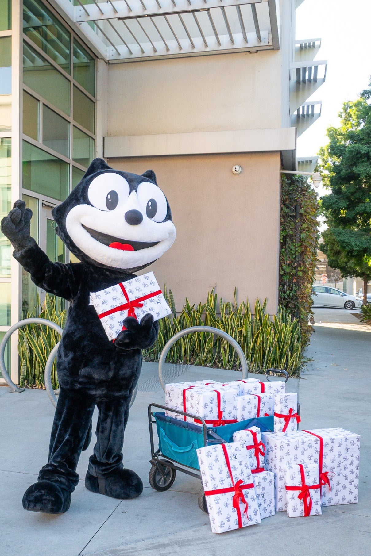 Felix mascot holding wrapped gifts in Felix branded wrapping paper