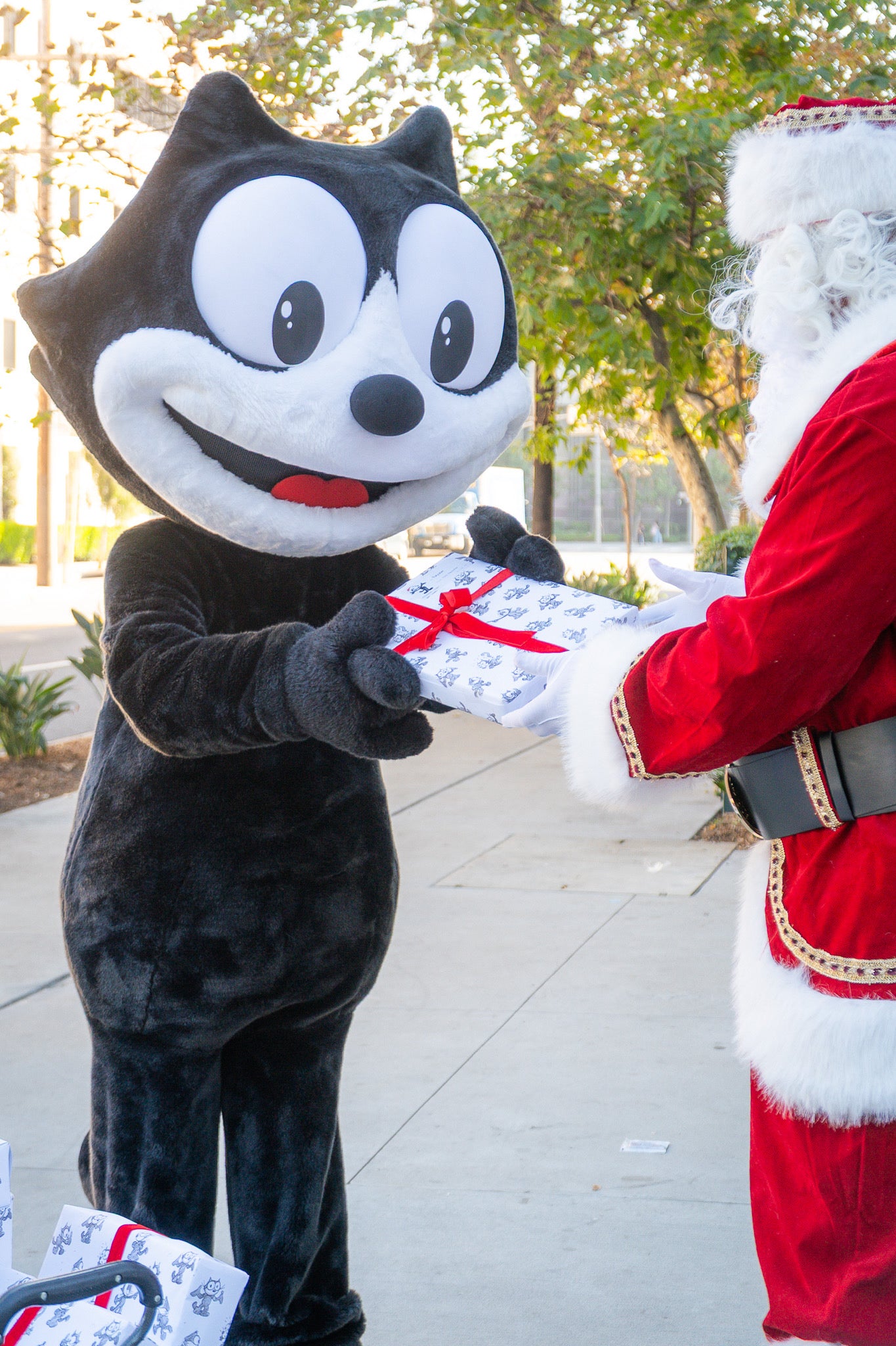 Felix mascot holding wrapped gifts in Felix branded wrapping paper