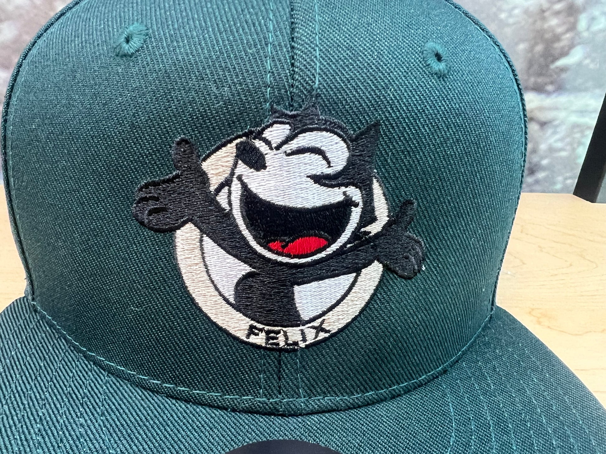 Closeup embroidery detail of smiling Felix The Cat on green flat bill hat